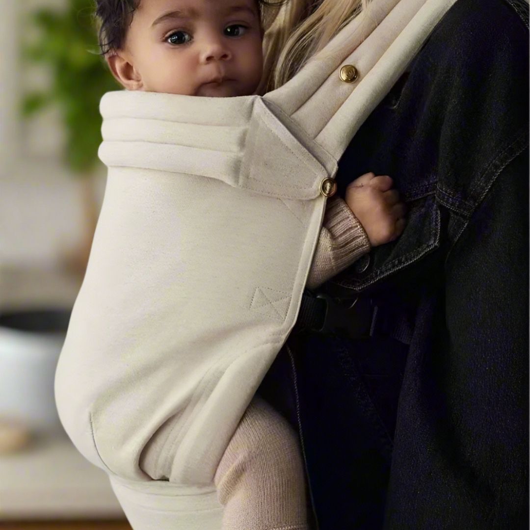 Une mère portant son bébé face à elle dans un porte bébé physiologique de couleur beige unie
