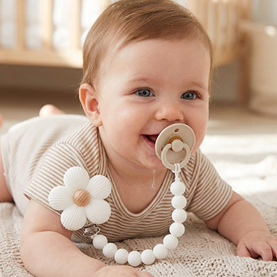 Attache tetine blanche en forme de fleur accrochée sur un bébé positionné sur le ventre