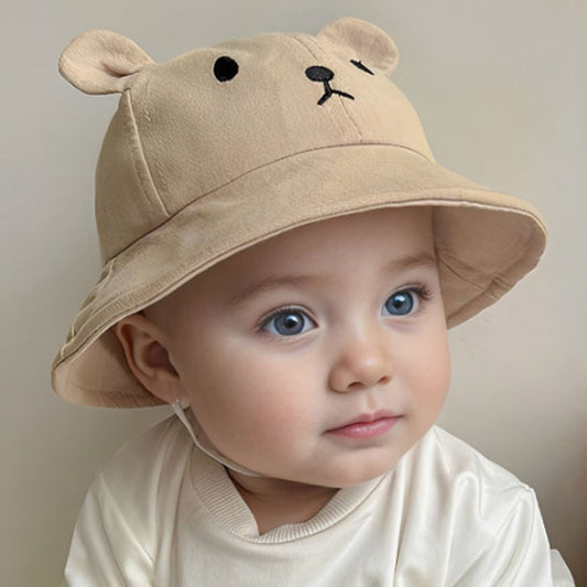 Chapeau bebe beige clair avec des oreilles de petit ours, avec un élastique de maintien poter sur la tête d'un jeune enfant