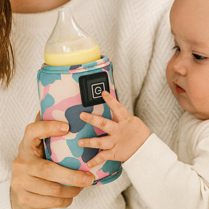 Un bébé dans les bras de sa maman tenant un biberon recouvert d'un chauffe-biberon portable