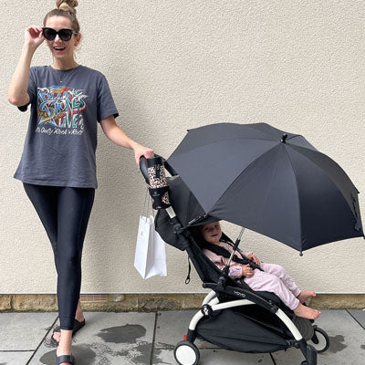 Une mère portant des lunettes de soleil avec son enfant dans une poussette muni d'une ombrelle pour poussette noire