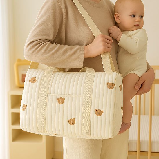 Sac à langer beige à motif petit ours porté en bandoulière.