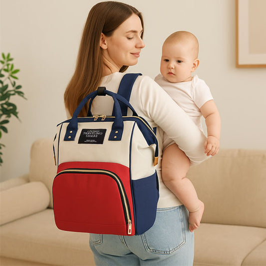 Mère de dos portant son bébé dans les bras avec un sac a langer sur les épaules de couleur bleu, blanc et rouge