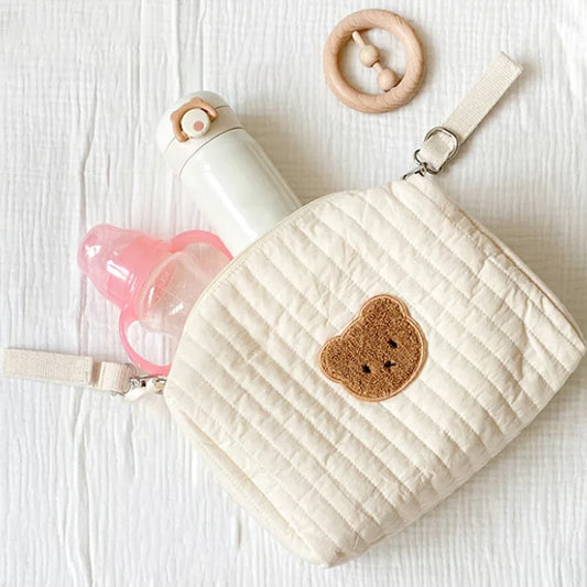 Trousse de toilette bebe beige avec un motif de tête d'ours sur le devant ouverte avec des produits bébé dedant