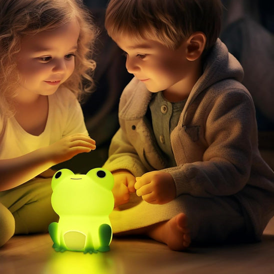 Deux enfants assis sur le sol, jouant avec leur veilleuse bébé grenouille verte illuminé 
