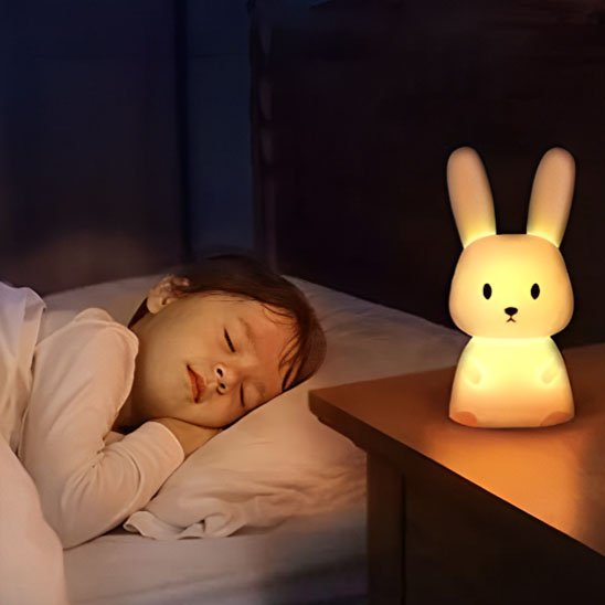 Veilleuse bébé lapin poser sur une table de chevet près d'un jeune garçon endormi