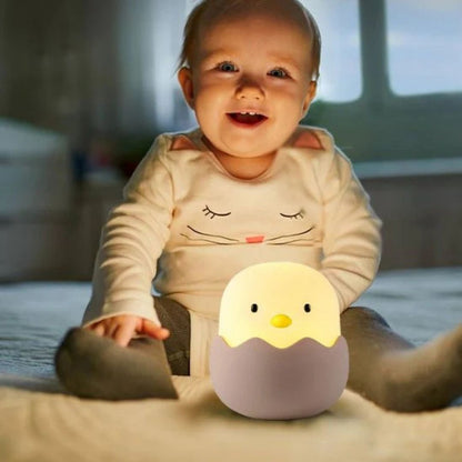 Bébé assis sur le sol de sa chambre avec une veilleuse bébé poussin face à lui
