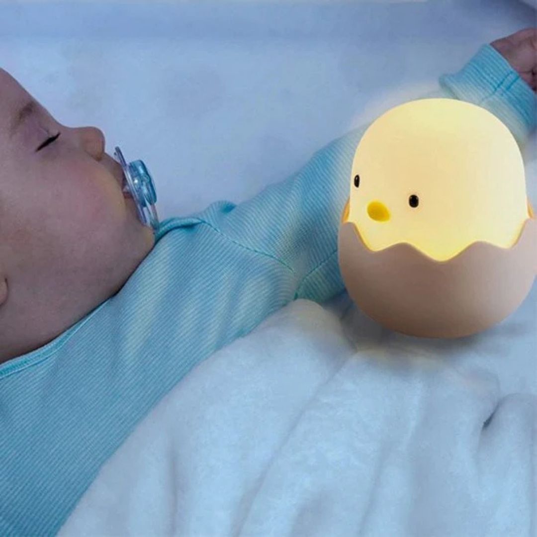 Bébé dormant dans son lit, avec sa tétine dans la bouche et sa veilleuse bébé poussin dans les bras