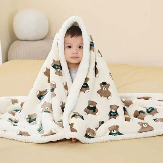 Enfant portant une couverture bébé sur les épaule beige clair avec des motifs de prtits oursons bruns